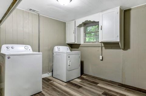 laundry area featuring washing machine and clothes dryer, visible vents, cabinet space, wooden walls, and wood finished floors