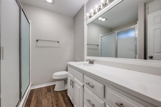 bathroom featuring toilet, wood finished floors, vanity, baseboards, and a stall shower