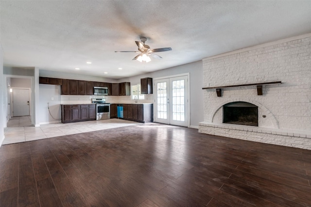 unfurnished living room featuring a ceiling fan, light wood-style flooring, a textured ceiling, a fireplace, and a sink