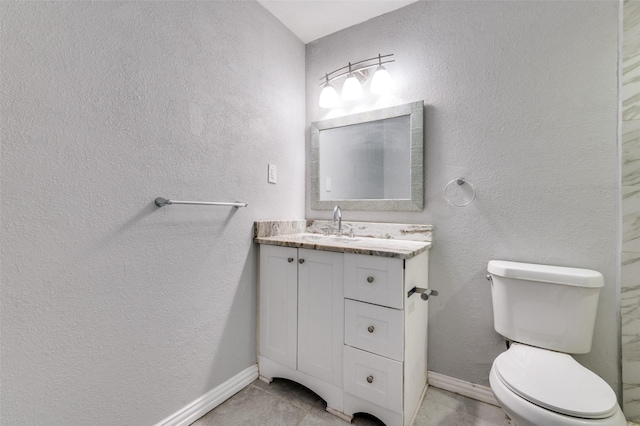 bathroom with a textured wall, vanity, toilet, and baseboards