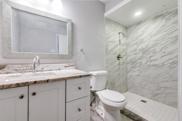 full bath featuring a textured wall, a tile shower, vanity, and toilet