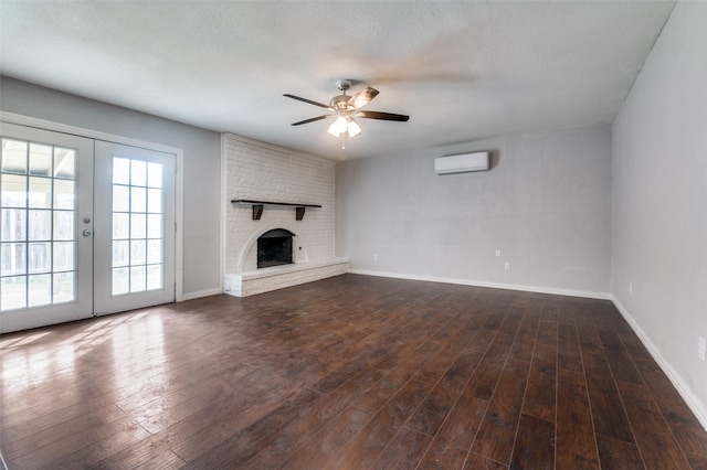 unfurnished living room featuring french doors, a wall mounted AC, dark wood-type flooring, a ceiling fan, and a brick fireplace