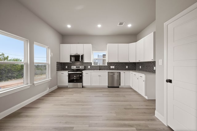 kitchen with light wood-style flooring, visible vents, baseboards, appliances with stainless steel finishes, and decorative backsplash