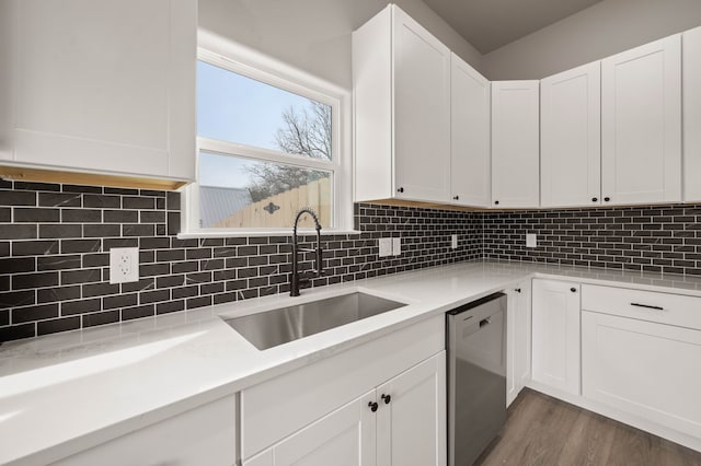 kitchen with stainless steel dishwasher, backsplash, a sink, and white cabinetry