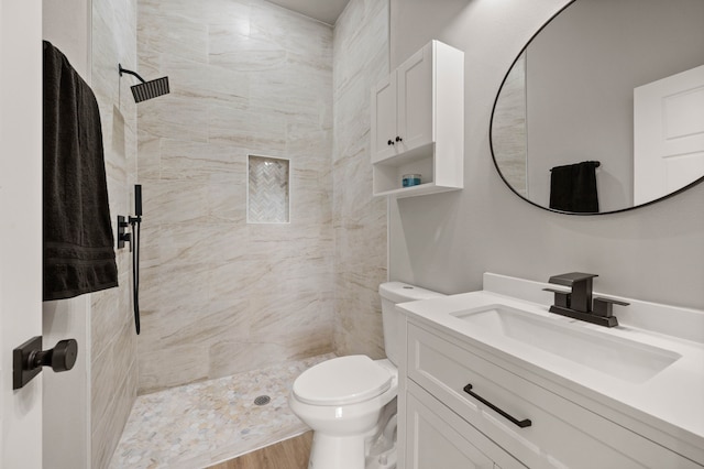 bathroom with toilet, a tile shower, wood finished floors, and vanity