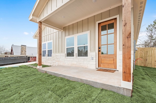 property entrance featuring fence, a yard, stone siding, board and batten siding, and a patio area