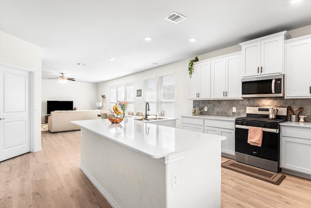 kitchen featuring light wood finished floors, visible vents, a kitchen island, appliances with stainless steel finishes, and a sink