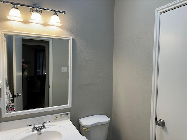 half bath featuring toilet, a textured wall, and vanity