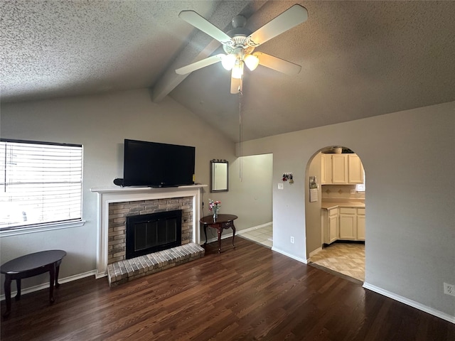 living area with arched walkways, lofted ceiling with beams, a fireplace, and wood finished floors