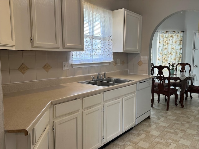 kitchen featuring arched walkways, decorative backsplash, white dishwasher, light countertops, and a sink