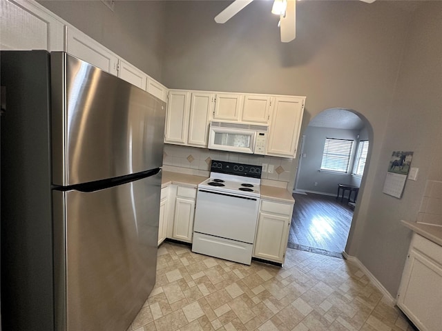 kitchen featuring arched walkways, white appliances, white cabinets, light countertops, and tasteful backsplash