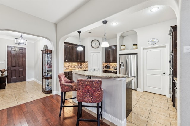 kitchen featuring a kitchen bar, a center island, arched walkways, dark brown cabinetry, and stainless steel fridge with ice dispenser