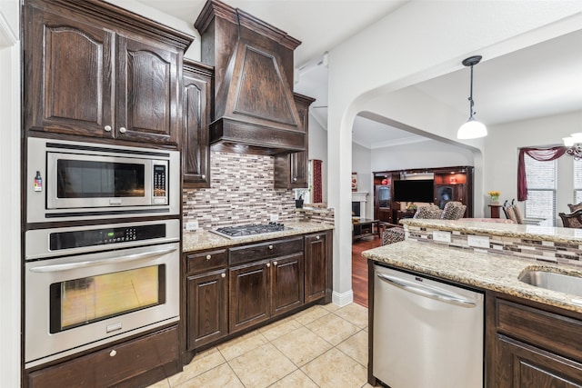 kitchen featuring dark brown cabinets, backsplash, premium range hood, light stone counters, and stainless steel appliances