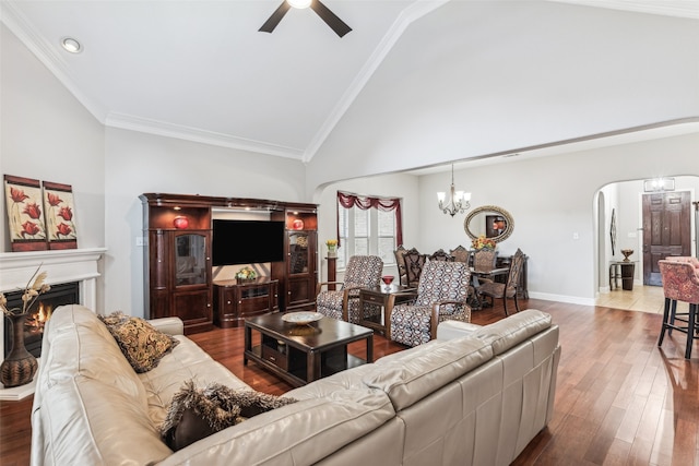 living room featuring crown molding, ceiling fan with notable chandelier, a warm lit fireplace, wood finished floors, and arched walkways