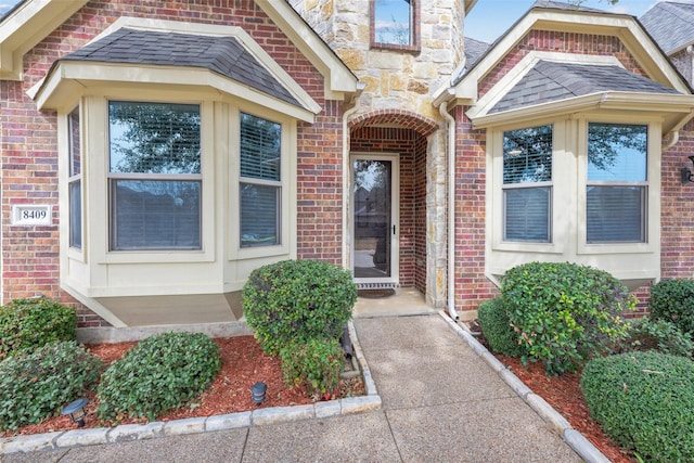 doorway to property featuring brick siding and a shingled roof