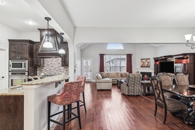 kitchen with dark wood-style flooring, dark brown cabinetry, appliances with stainless steel finishes, a kitchen bar, and tasteful backsplash