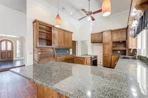 kitchen with a peninsula, a sink, a towering ceiling, open shelves, and brown cabinetry