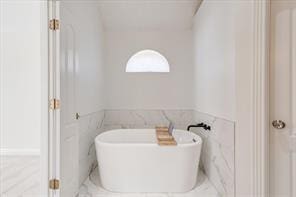 bathroom with a tub to relax in, a wainscoted wall, and tile walls