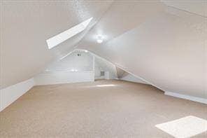 bonus room featuring vaulted ceiling with skylight and carpet flooring