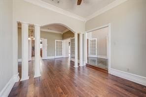 empty room featuring ceiling fan, wood finished floors, baseboards, decorative columns, and crown molding