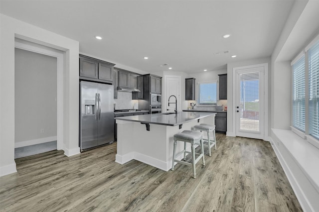 kitchen with a breakfast bar area, light wood finished floors, stainless steel appliances, visible vents, and a sink