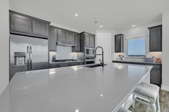 kitchen with stainless steel appliances, visible vents, decorative backsplash, a sink, and a kitchen bar