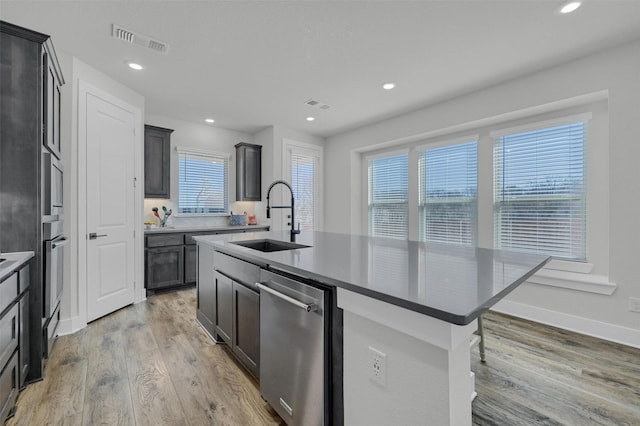 kitchen with a center island with sink, stainless steel appliances, visible vents, light wood-style floors, and a sink