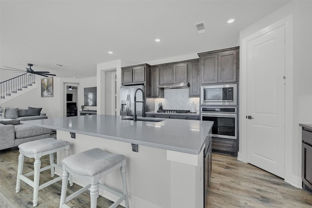 kitchen with tasteful backsplash, open floor plan, stainless steel appliances, light wood-type flooring, and a sink