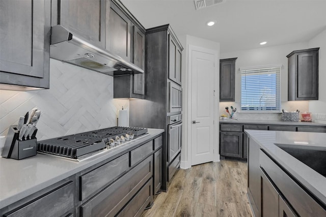 kitchen with under cabinet range hood, stainless steel appliances, visible vents, light countertops, and light wood finished floors