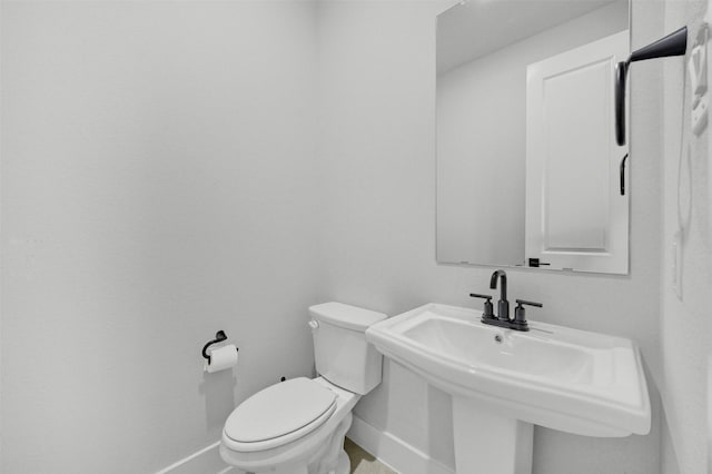 half bathroom with a sink, toilet, and baseboards