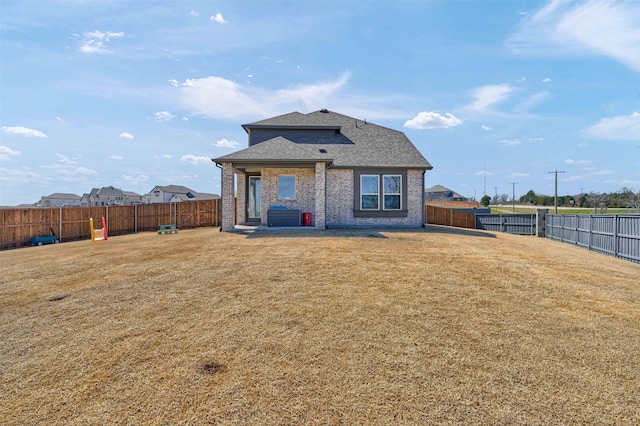 rear view of property featuring brick siding, a yard, and a fenced backyard