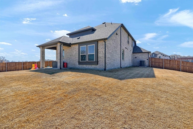 rear view of house with brick siding, a fenced backyard, central AC, and a yard