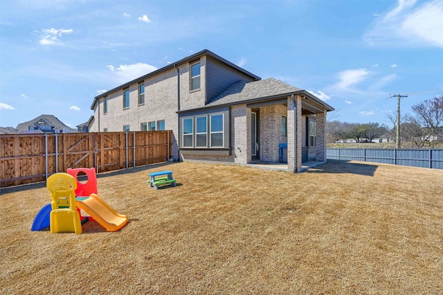 back of property with brick siding, a lawn, a fenced backyard, and a playground