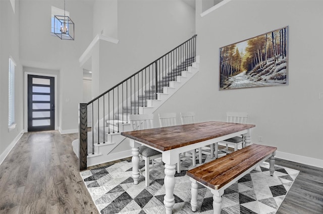 dining space featuring a towering ceiling, stairway, wood finished floors, a chandelier, and baseboards