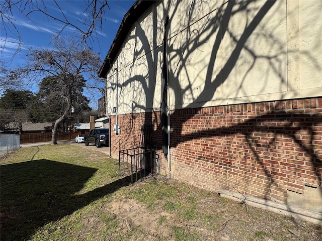 view of side of home with a yard, fence, and brick siding