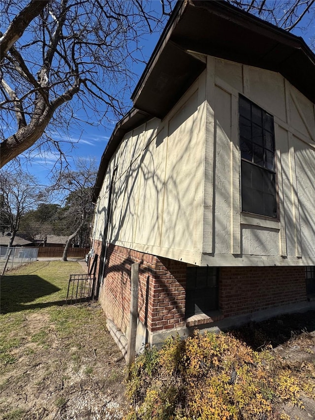 view of side of home featuring fence, a lawn, and brick siding