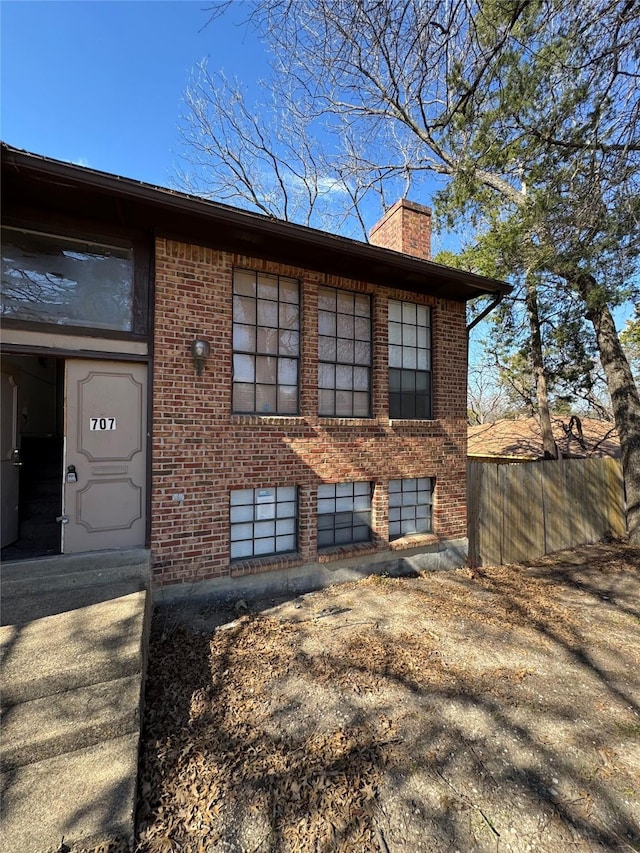 exterior space featuring a chimney, fence, and brick siding