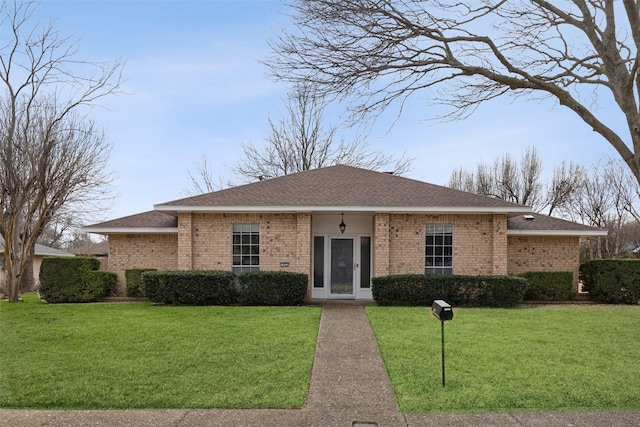 view of front of house featuring a shingled roof, a front yard, and brick siding