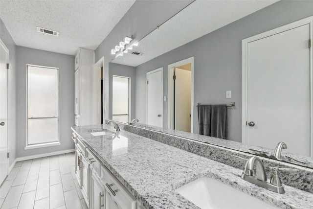 bathroom featuring a textured ceiling, a sink, and visible vents