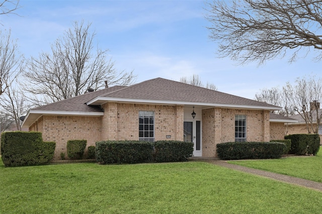 view of front facade with brick siding, a front lawn, and a shingled roof