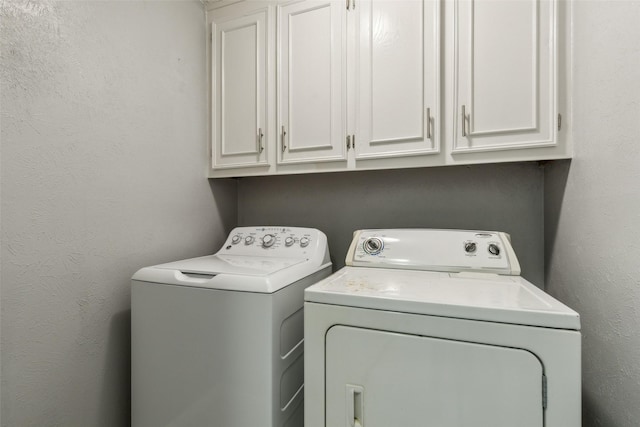 washroom with a textured wall, independent washer and dryer, and cabinet space