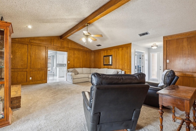 carpeted living area with vaulted ceiling with beams, a textured ceiling, visible vents, and wooden walls