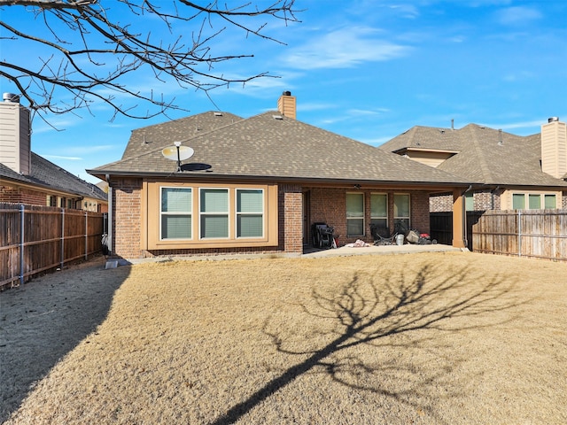 back of property featuring a shingled roof, a chimney, brick siding, and a fenced backyard