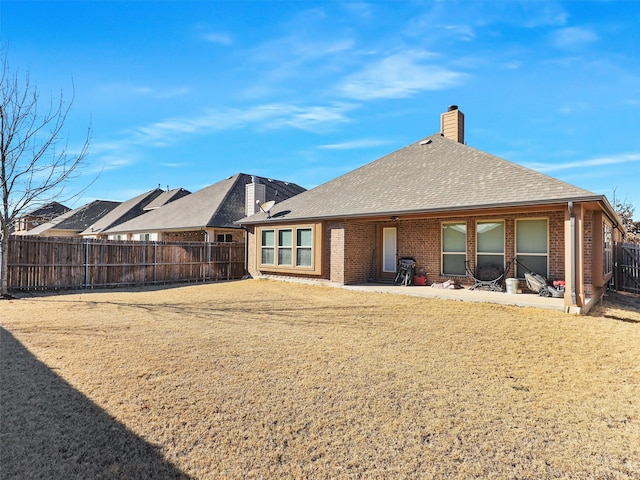 back of property with a shingled roof, a patio, a fenced backyard, a chimney, and brick siding