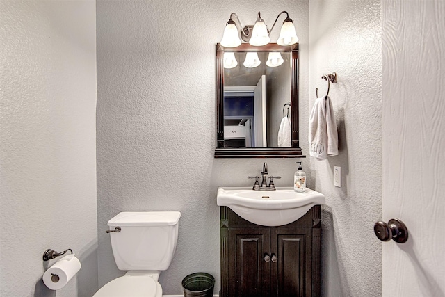 half bathroom featuring toilet, a textured wall, and vanity