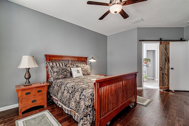 bedroom featuring visible vents, a barn door, a textured ceiling, baseboards, and hardwood / wood-style flooring