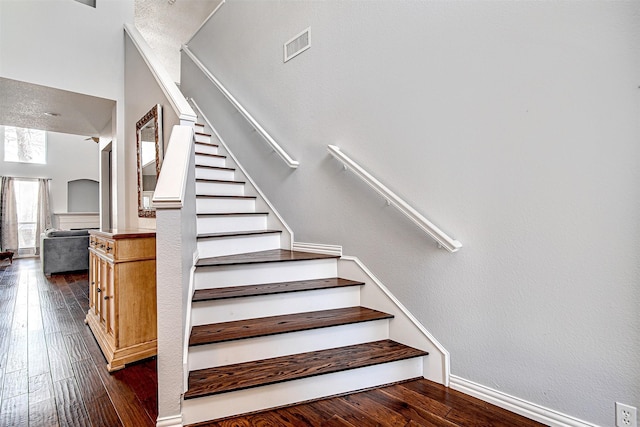 stairs with wood-type flooring, visible vents, and a textured wall