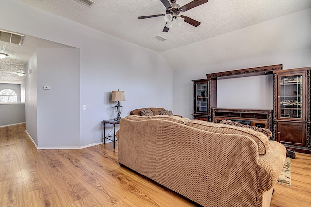 living room with light wood-type flooring, a ceiling fan, visible vents, and a textured ceiling