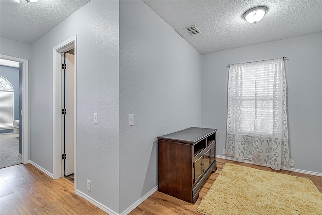 hall with light wood-style floors, baseboards, visible vents, and a textured ceiling