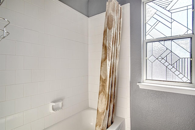 bathroom with a textured wall, shower / bath combination with curtain, and a wealth of natural light